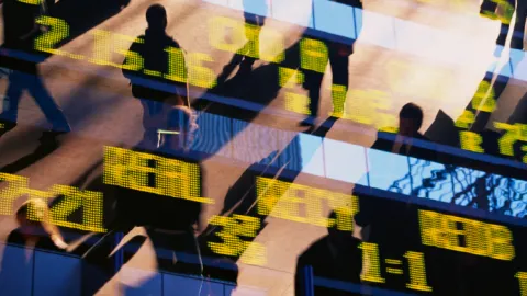 Silhouettes of people walking past a digital display with yellow numbers and data overlays, symbolizing financial activity and fraud monitoring. 